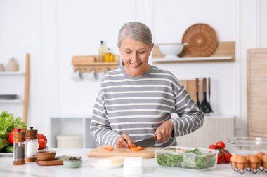 Üst düzey kadın mutfaktaki beyaz mermer masada yemek pişiriyor.