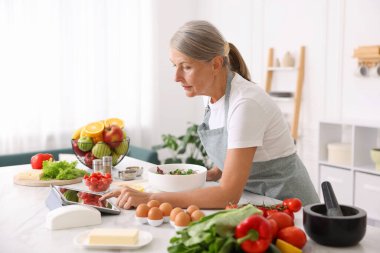 Üst düzey kadın mutfakta beyaz mermer masada salata pişirirken tablet kullanıyor.