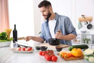 Mutfakta yemek pişirirken tabletten yemek tarifine bakan genç bir adam.