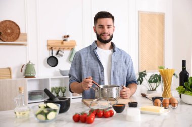 Mutfaktaki masada yemek pişiren gülümseyen adam.