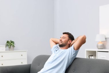 Happy man resting on sofa at home. Space for text