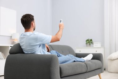 Evdeki kanepede uzaktan kumandayla klima kullanan bir adam. Metin için boşluk