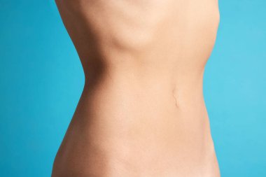 Açık mavi arka planda düz göbekli kadın, yakın plan.