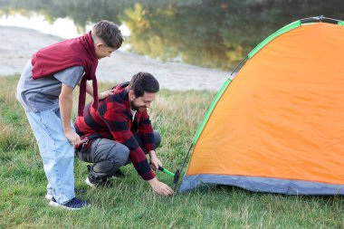 Mutlu baba ve oğul nehir kenarında kamp çadırı kuruyorlar.