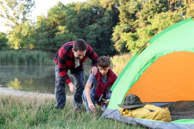 Baba ve oğul nehir kenarında kamp çadırı kuruyorlar.