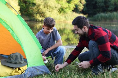 Baba ve oğul nehir kenarında kamp çadırı kuruyorlar.