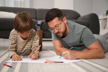 Baba ve oğul evde yerde birlikte çiziyorlar.