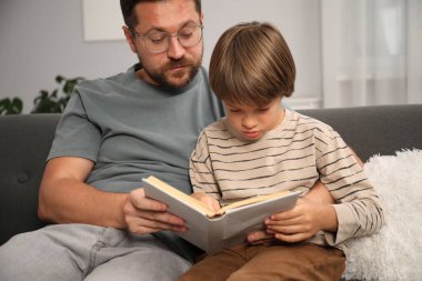 Baba ve oğul evdeki kanepede kitap okuyorlar.