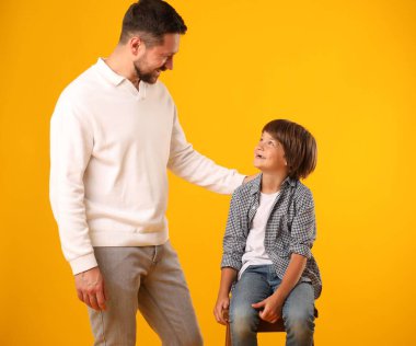 Baba ve oğul sarı arka planda poz veriyorlar.