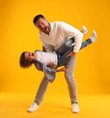 Baba ve oğul sarı arka planda eğleniyorlar.