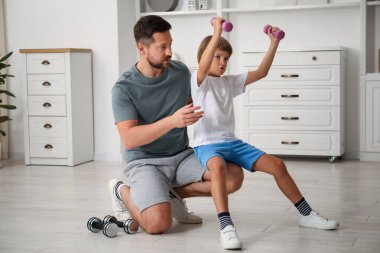 Baba oğul evde dambıllarla antrenman yapıyor.