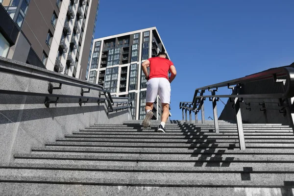 Spor kıyafetli bir adam merdivenlerde koşuyor, alçak açılı.