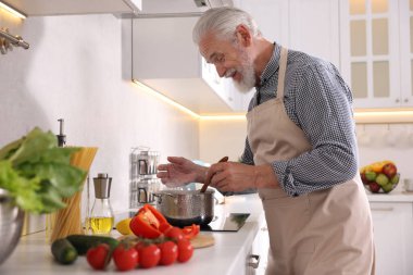 Mutfaktaki mutfağın tepesinde yaşlı bir adam yemek pişiriyor.