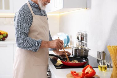 Mutfaktaki mutfağın tepesinde yemek pişiren yaşlı adam, yakın plan.