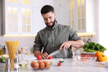 Yemek pişirme süreci. Gülümseyen adam mutfakta domates kesiyor.