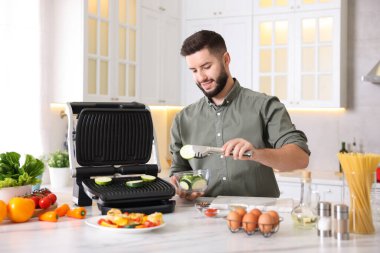 Gülümseyen adam mutfaktaki masada kabak pişiriyor.