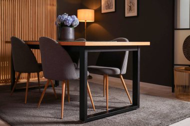 Geceleri yemek odasında güzel çiçekler ve sandalyeler olan ahşap masa.