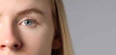 Açık gri arka planda güzel gözleri olan bir kadın, yakın plan. Metin için boşluk