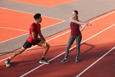 Spor giyimli bir çift stadyumda koşmadan önce ısınma egzersizleri yapıyor.