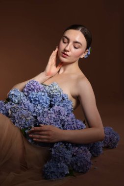 Kahverengi arka planda hortensiya çiçekleri olan güzel genç bir kadın.