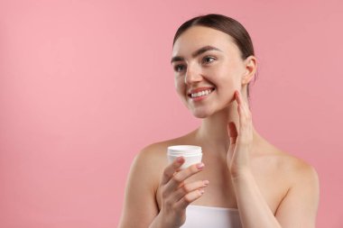 Güzel bir kadın pembe arka planda yüzüne krem sürüyor. Metin için boşluk
