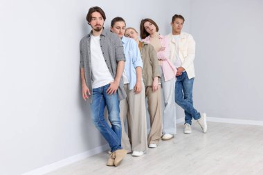 Açık gri duvarın yanında bir grup insan bekliyor.