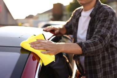 Dışarıdaki sarı mikrofiber bez parçasıyla araba silen adam, yakın plan.