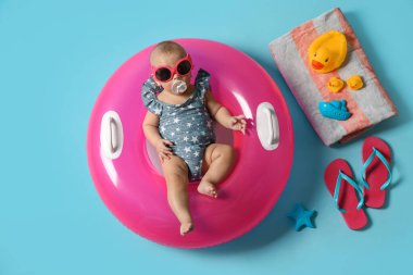 Güneş gözlüklü şirin bir bebek. Şişirilebilir yüzüğü ve açık mavi arka planda plaj aksesuarları var.
