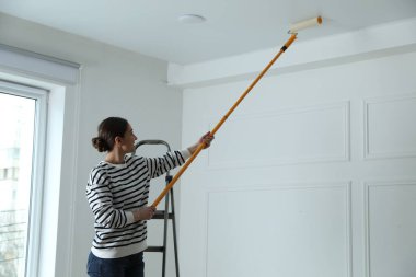 Tavanı beyaz boyayla boyayan genç bir kadın.