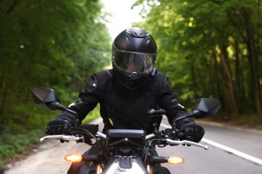 Kasklı genç adam modern motosikleti açık havada kullanıyor.