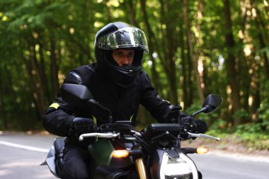 Kasklı genç adam modern motosikleti açık havada kullanıyor.