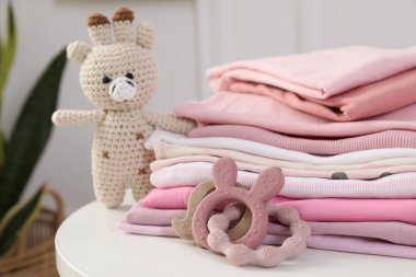 İçerideki beyaz masada temiz bebek kıyafetleri ve oyuncaklar yığını, yakın plan.