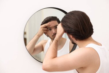 Evinde aynanın yanında sivilce sorunu olan genç bir adam var.