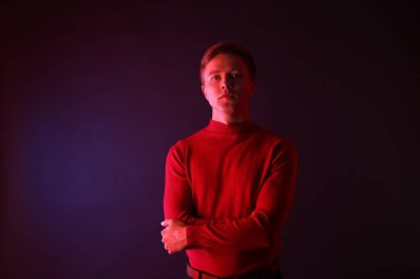 Koyu arkaplanda neon ışıkları altında çapraz kollu yakışıklı bir adamın portresi.