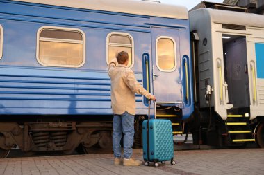 Hoşçakalın. Bagajlı bir adam trenin yanında el sallıyor.