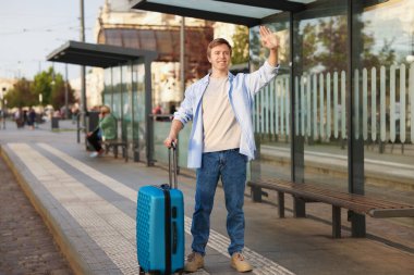 Hoşçakalın. Bagajlı adam otobüs durağında el sallıyor.