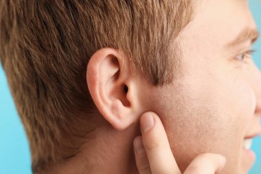 Ses geliyor. Açık mavi arka plandaki adam, yakın plan.