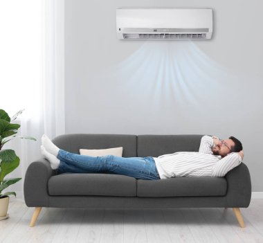 Evdeki kanepede dinlenen mutlu adam. Klima odada rahat bir sıcaklık sağlıyor.