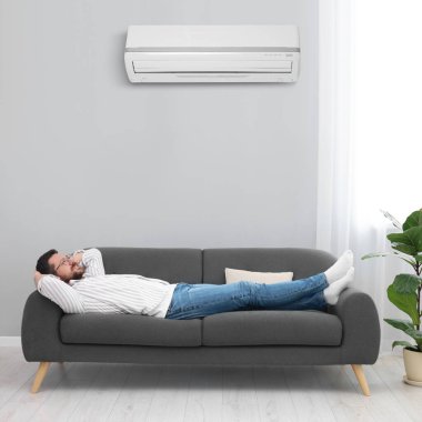 Evdeki kanepede dinlenen mutlu adam. Klima odada rahat bir sıcaklık sağlıyor.