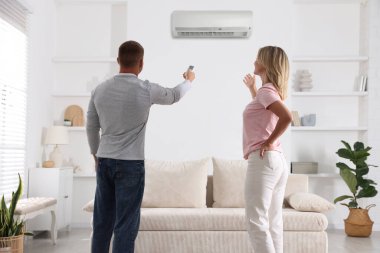 Kadın ve erkek evdeki klimayı kontrol etmek için uzaktan kumanda kullanıyor.