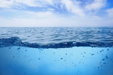 Deniz suyu yüzeyi ve su altı manzarası. Gökyüzü bulutlu