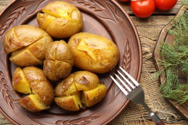 Lezzetli fırında patates, çatal, dereotu ve domatesler ahşap masada, düz yerde.