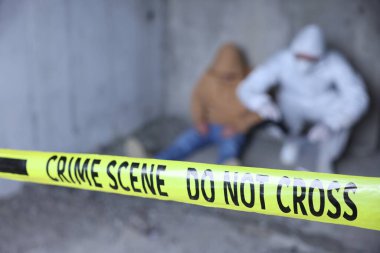 Adli tıp uzmanı terk edilmiş binanın içinde cesetle birlikte olay yerinde çalışıyor. Sarı polis bandına odaklan.