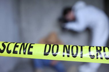 Adli tıp uzmanı terk edilmiş binanın içinde cesetle birlikte olay yerinde çalışıyor. Sarı polis bandına odaklan.