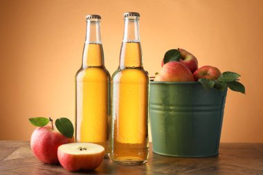 Cam şişelerde lezzetli elma şarabı ve ahşap masada portakal eğimli arka planda elmalar.