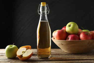 Cam şişede nefis elma şarabı ve ahşap masada koyu gri arka planda elmalar