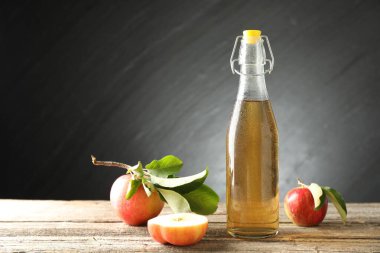 Cam şişede nefis elma şarabı ve ahşap masada koyu gri arka planda elmalar. Metin için boşluk