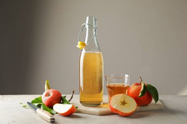 Şişede nefis elma şarabı, cam ve elmalar gri masada, arka planda ışığa karşı.