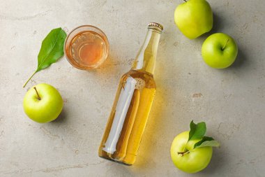 Şişede nefis elma şarabı, yeşil yapraklı cam ve elmalar gri desenli masa, düz uzanmış