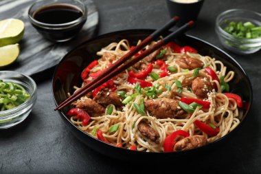 Siyah masada servis edilen tavuk, yeşil soğan ve sebzeli erişte, yakın plan.